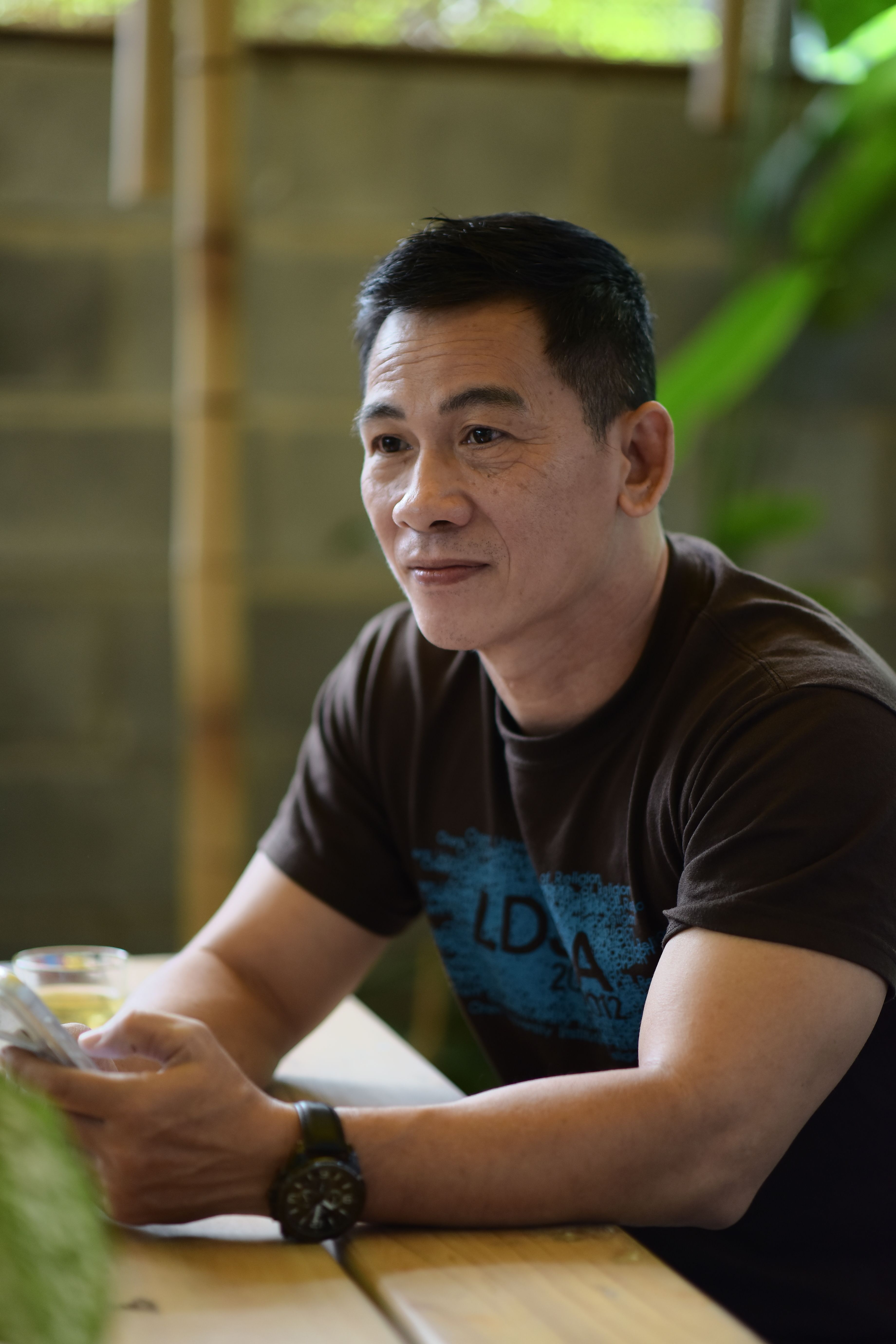 Man sitting in a cafe holding a smartphone, appearing thoughtful and relaxed.