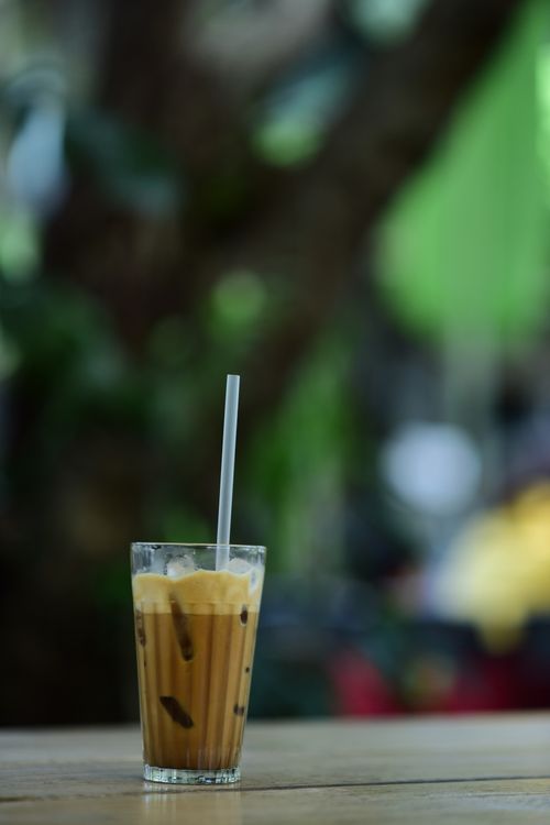Free Close-up of iced coffee with a straw, outdoors on a wooden table with a blurred natural background. Stock Photo