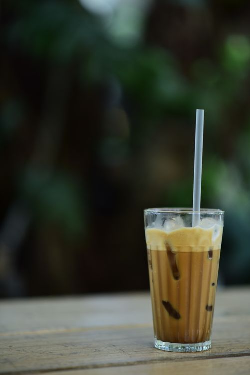 Free A glass of iced coffee with a straw on a wooden table, captured in natural light. Stock Photo
