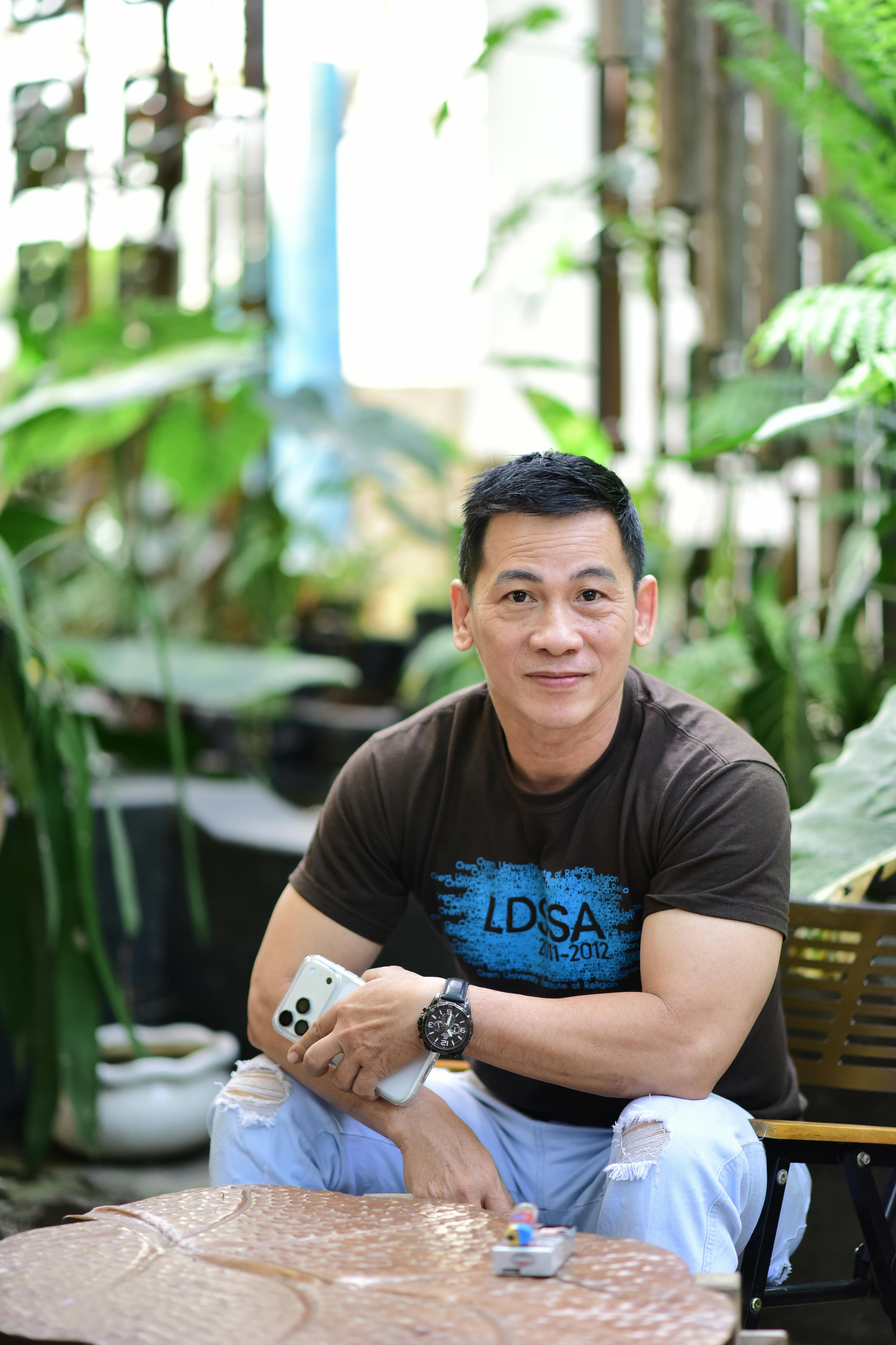 Smiling man seated in a lush garden, holding a smartphone.