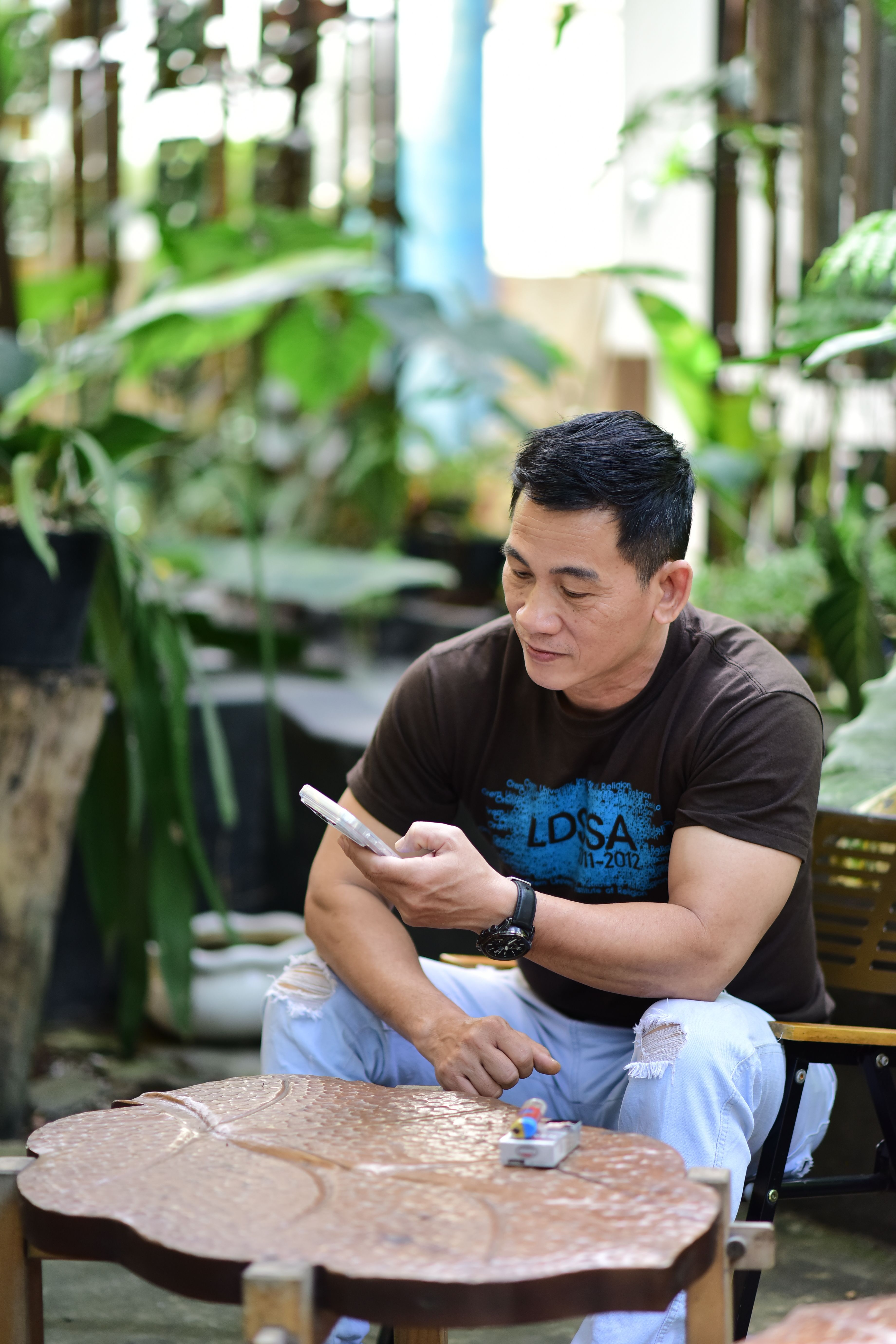 Man sitting outdoors in a garden, looking at his smartphone, creating a relaxed atmosphere.