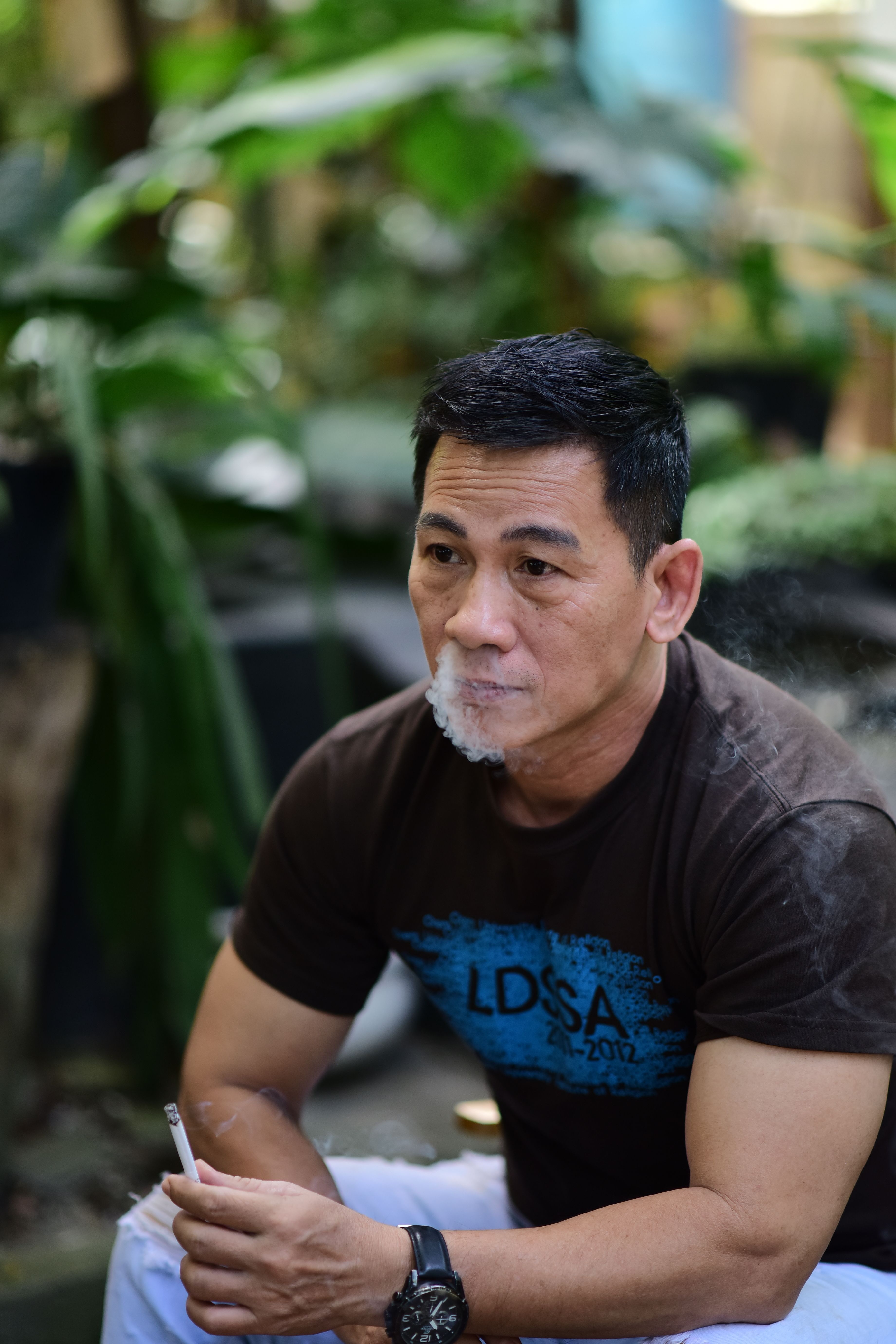 Contemplative man smoking outside surrounded by lush greenery.