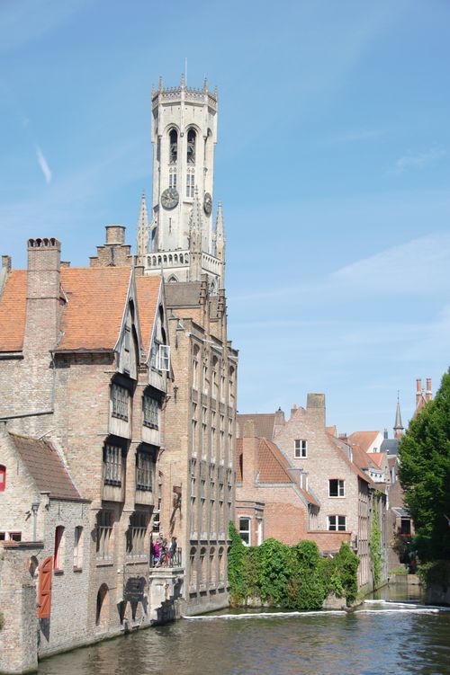 Free Charming scene of medieval architecture along a canal in Bruges with the iconic Belfry tower. Stock Photo