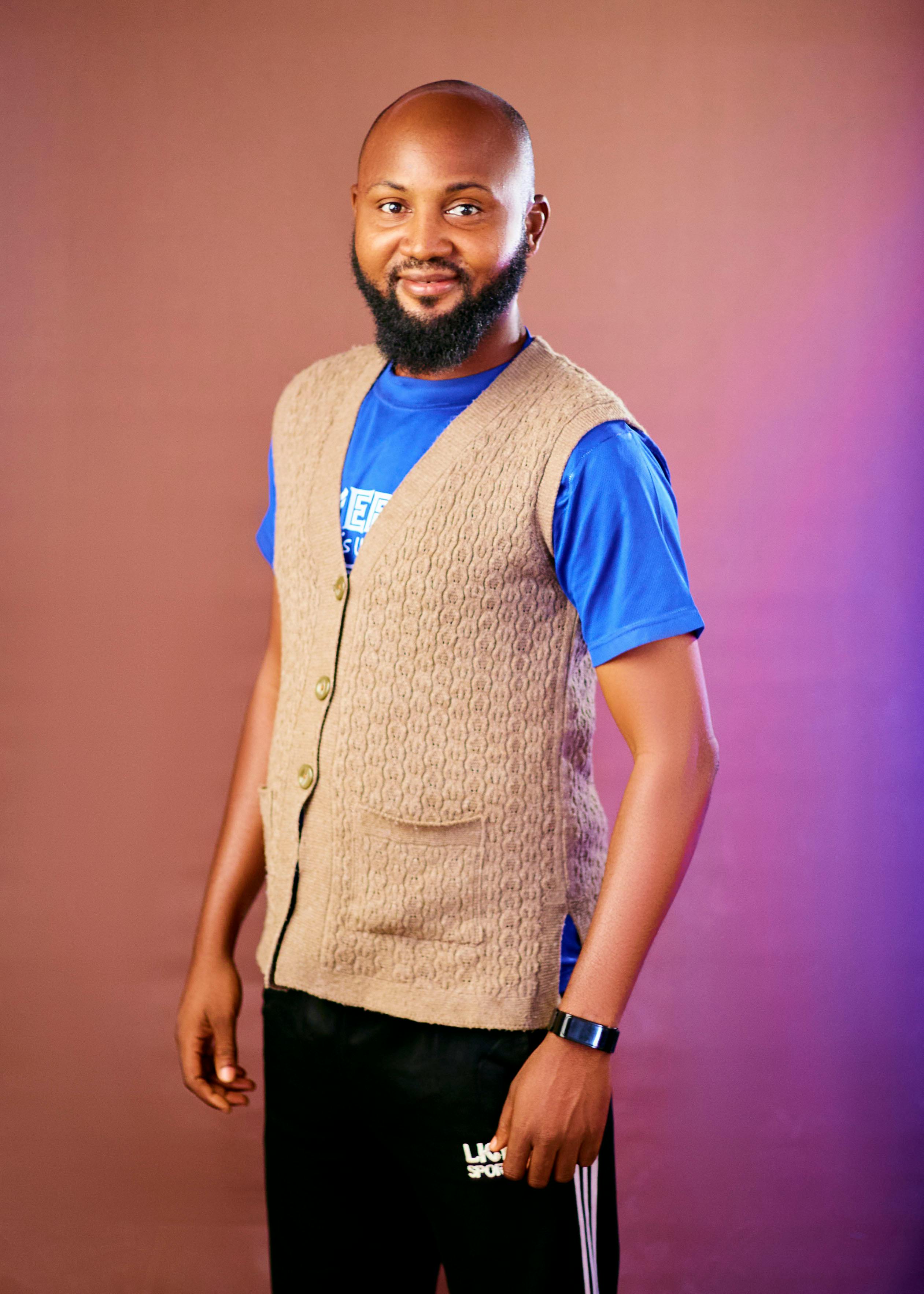 Portrait of a smiling man in a blue t-shirt and beige vest, posing confidently.