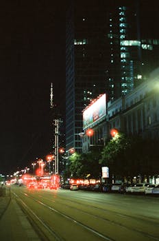 A vibrant night scene in Warsaw showcasing illuminated city streets and skyscrapers.