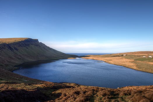 Vast lake in Scottish Highlands surrounded by rugged terrain under clear blue sky.