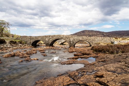 Free Rustic stone bridge crossing a scenic river in the Scottish Highlands. Stock Photo