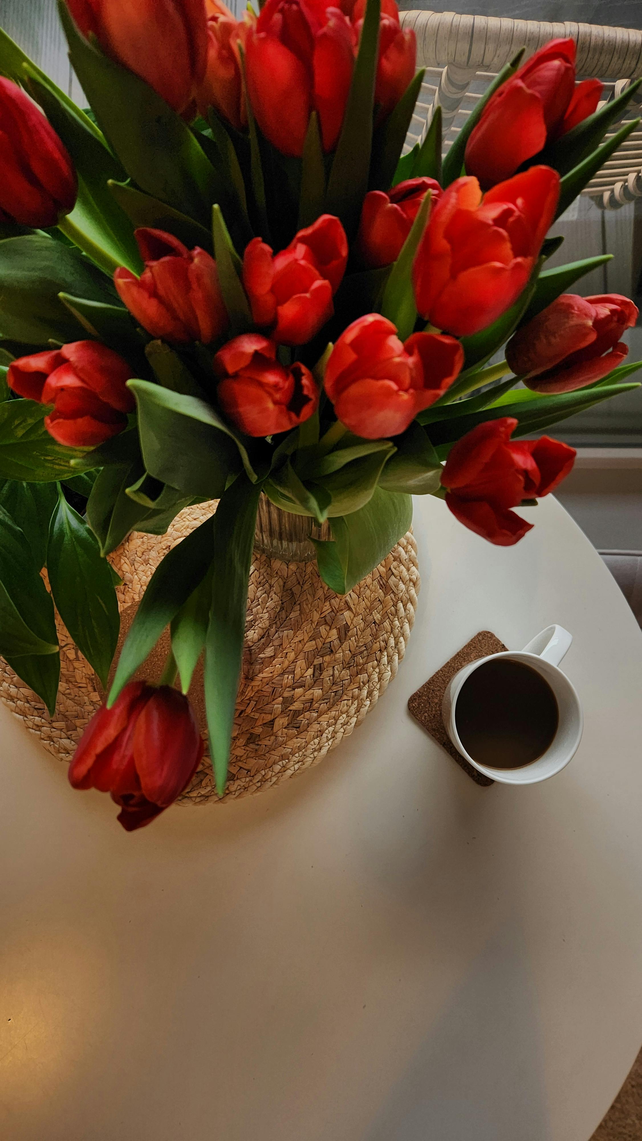 A beautiful bouquet of red tulips in a vase with a cup of coffee on a white table.