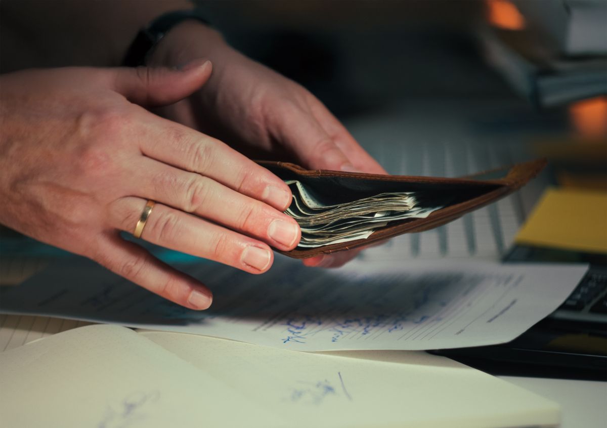 Pessoa segurando carteira com dinheiro enquanto analisa documentos