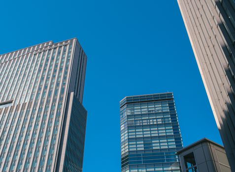 Dynamic view of modern skyscrapers rising against a clear blue sky, showcasing urban architecture.