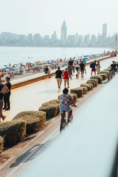 Beachfront promenade bustling with people and city skyline in the background.