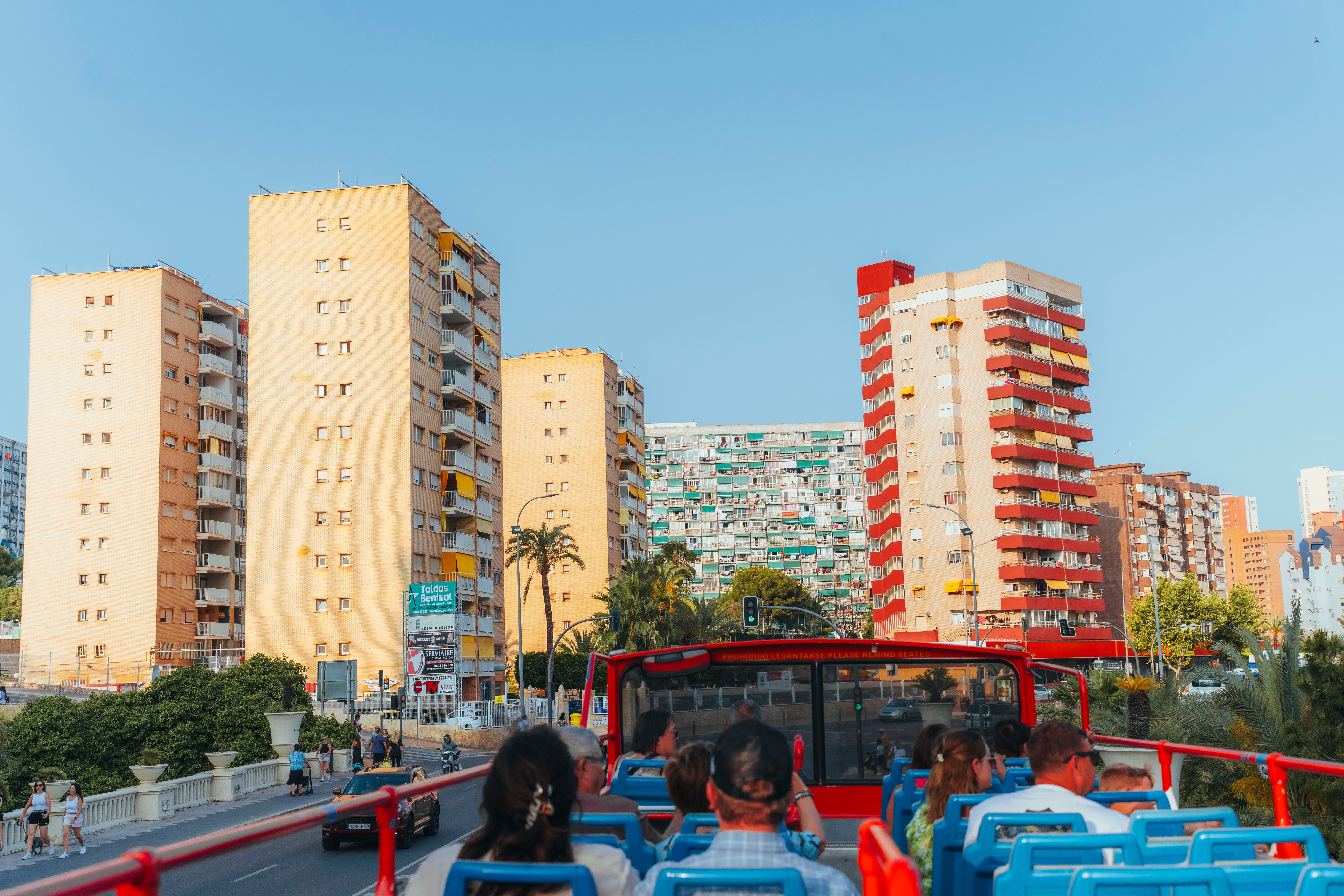 Tourists on an open-top bus tour enjoying a sunny day in a vibrant city with tall buildings.