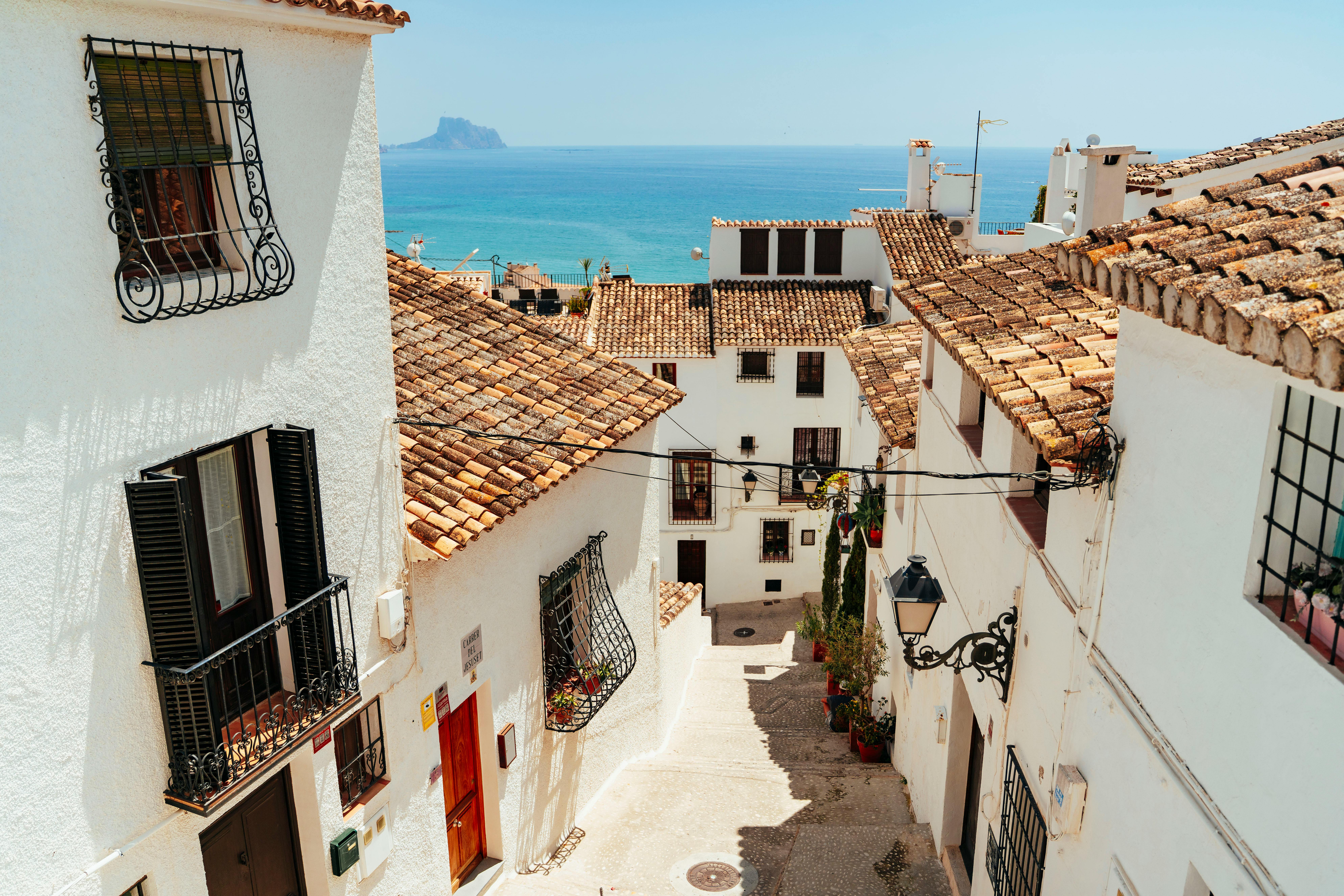 Picturesque Mediterranean alley with white houses and a stunning ocean view under a clear blue sky.