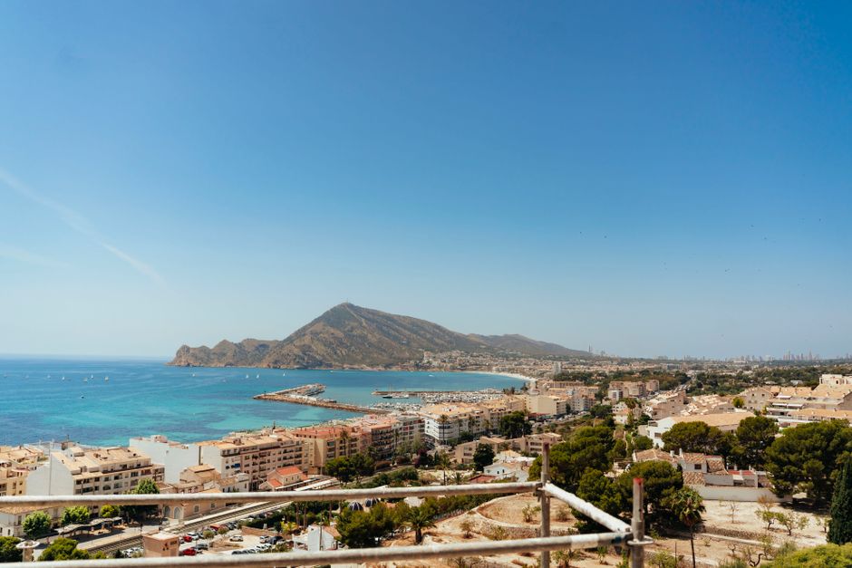 Aerial view of Altea's picturesque coastline, marina, and cityscape with blue skies and mountains.