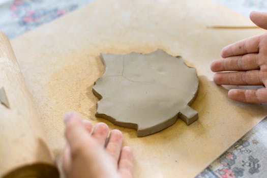 Hands shaping clay into a leaf design, showcasing pottery techniques.