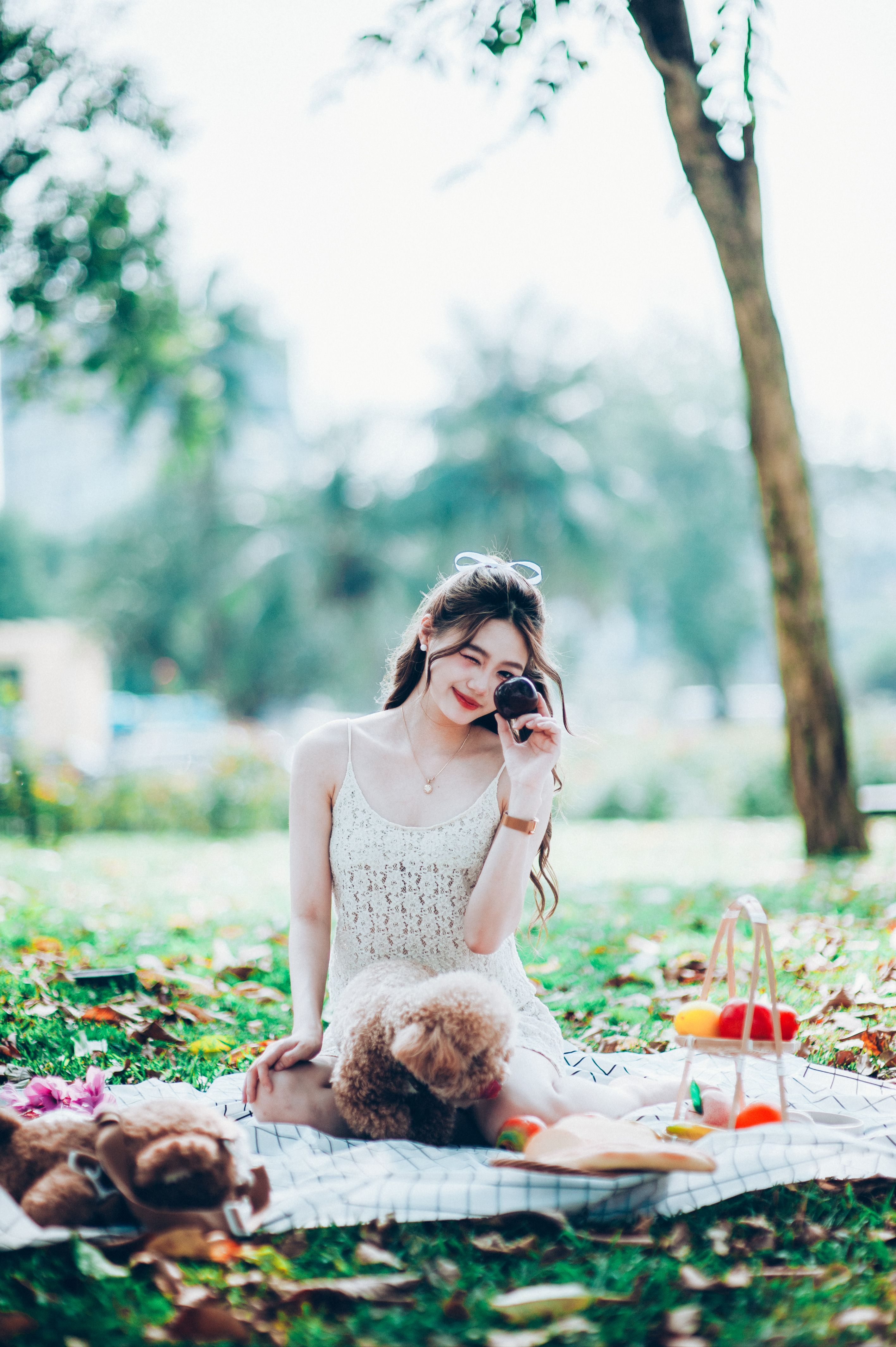 Young woman sitting on blanket during picnic with plush bear and fruits in the park.