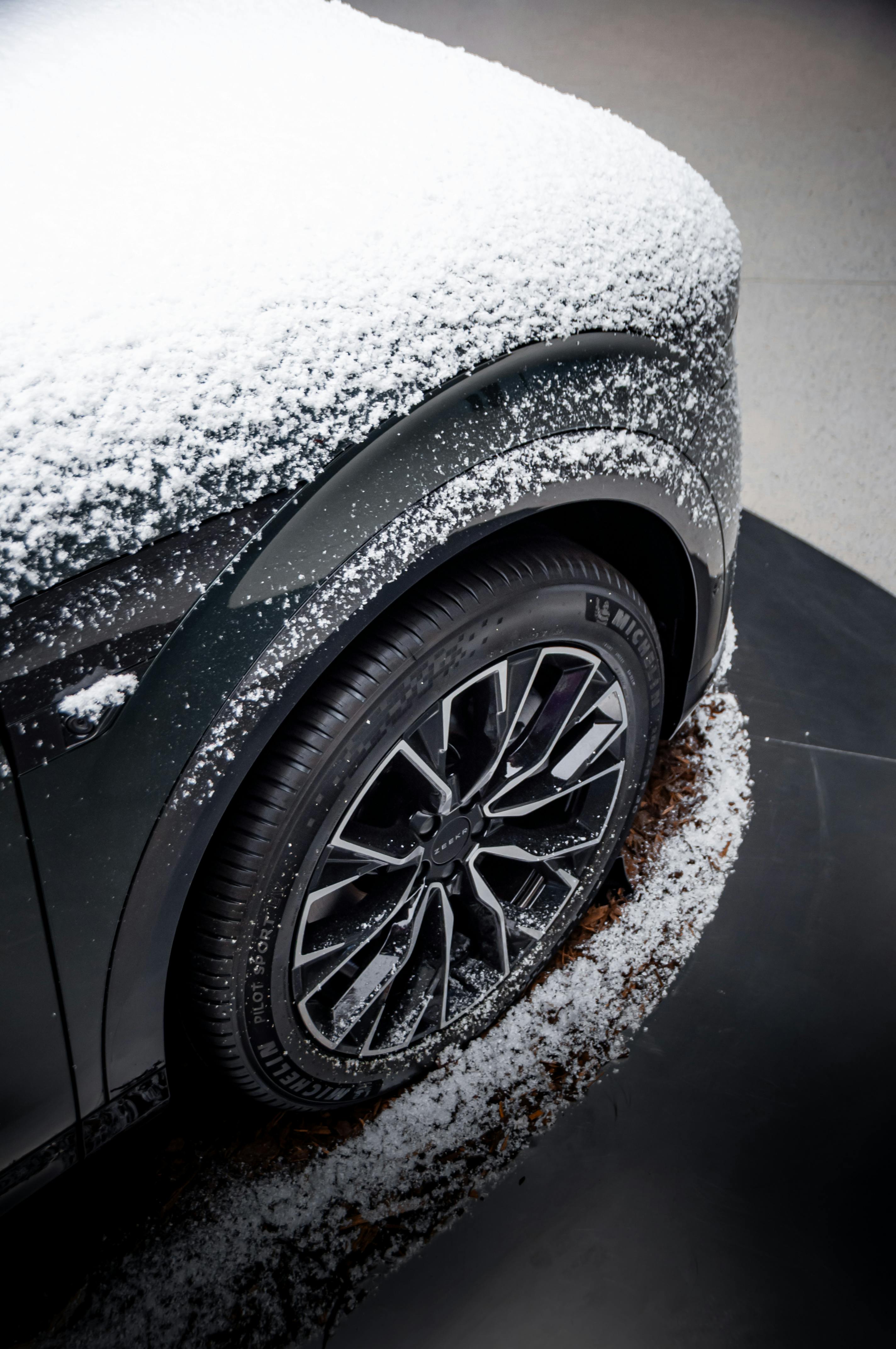 Close-up of a snow-covered car wheel showcasing modern design and winter atmosphere in an urban setting.