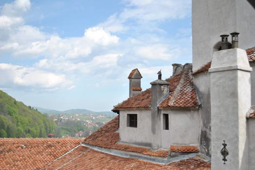 A picturesque castle rooftop overlooks a mountain landscape under a bright sky.