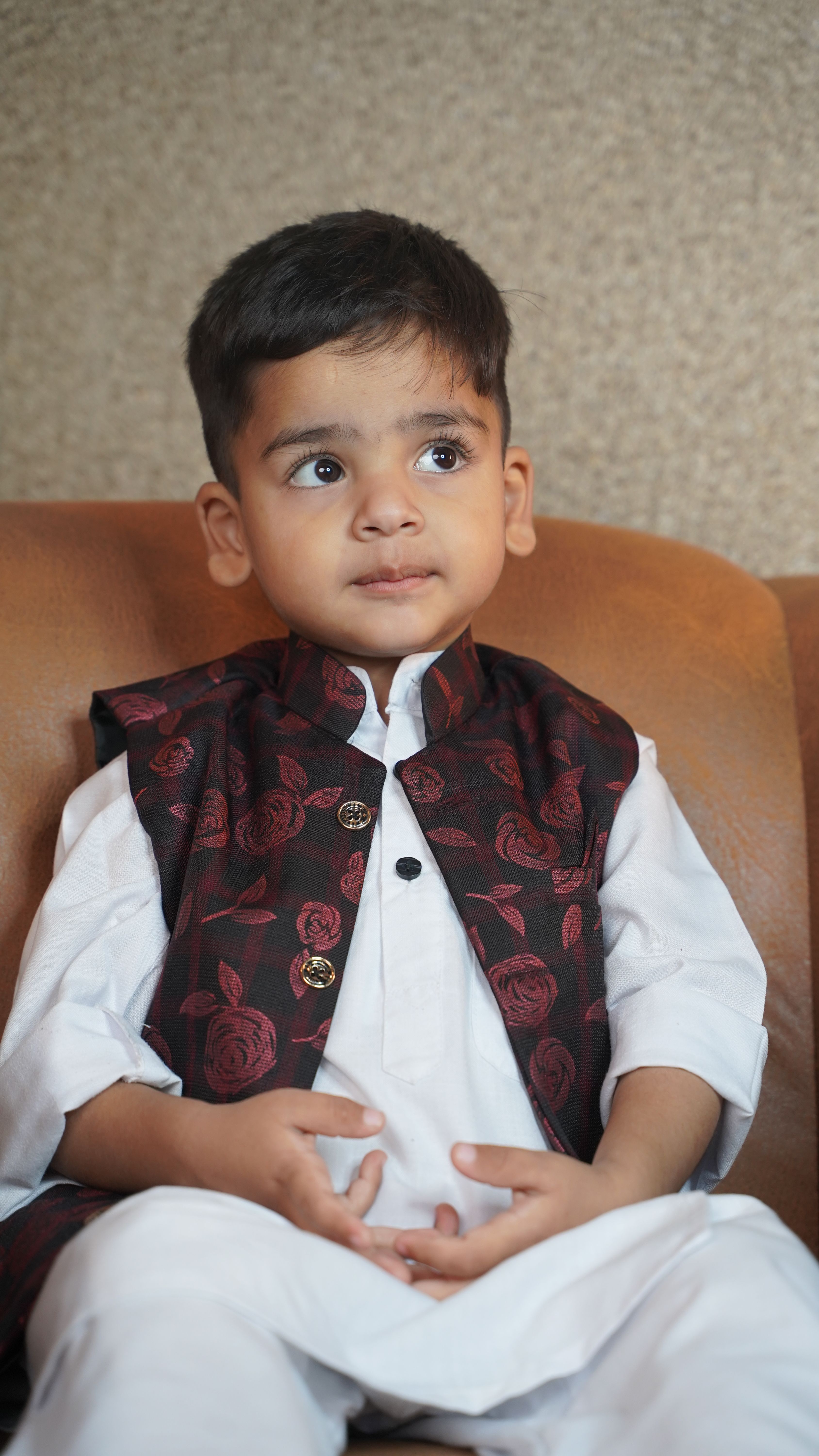 Portrait of a young boy wearing traditional Kashmiri clothing, thoughtfully gazing indoors. Captured in detail.