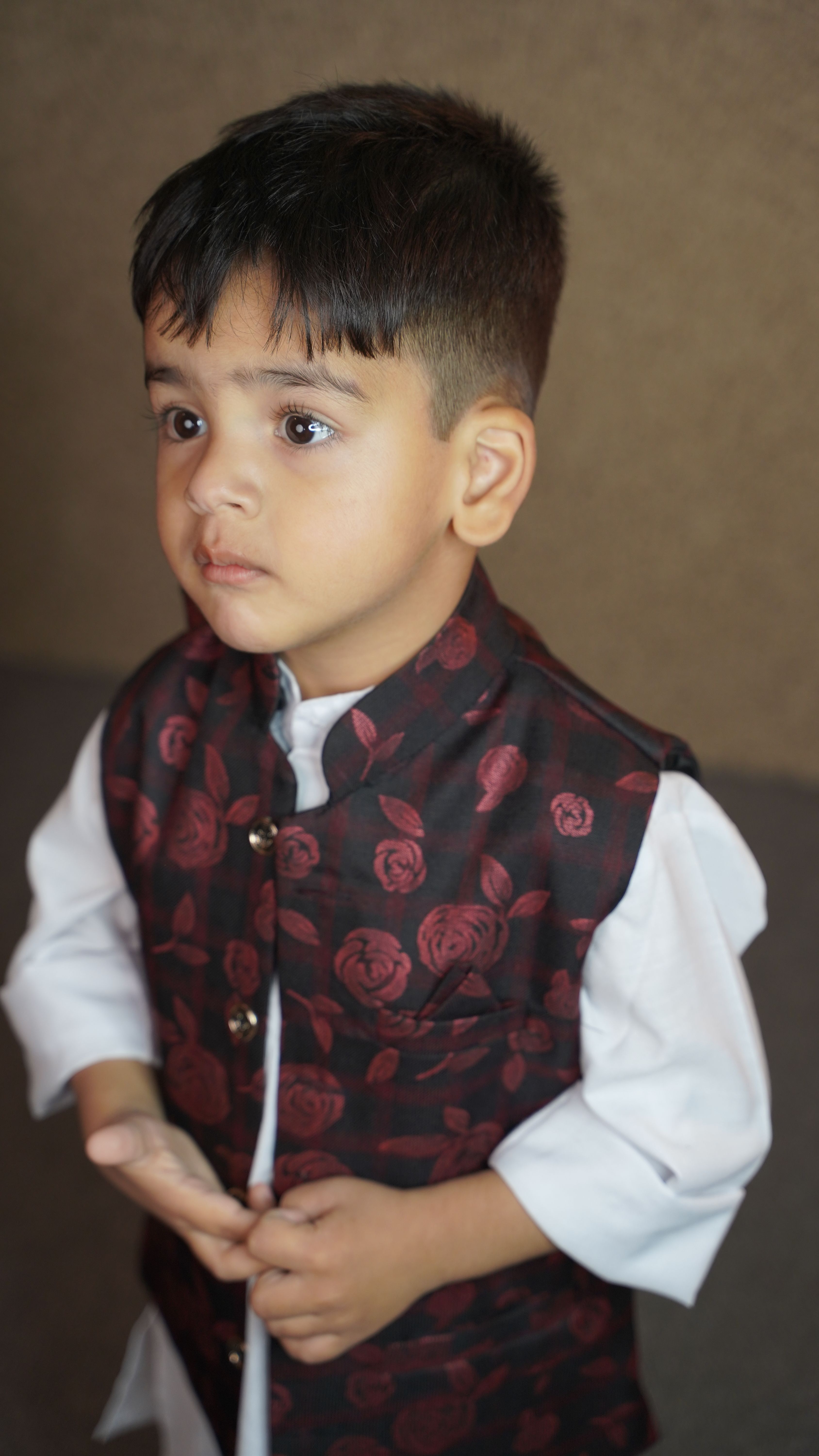 A young boy dressed in traditional South Asian clothing, looking thoughtful indoors.
