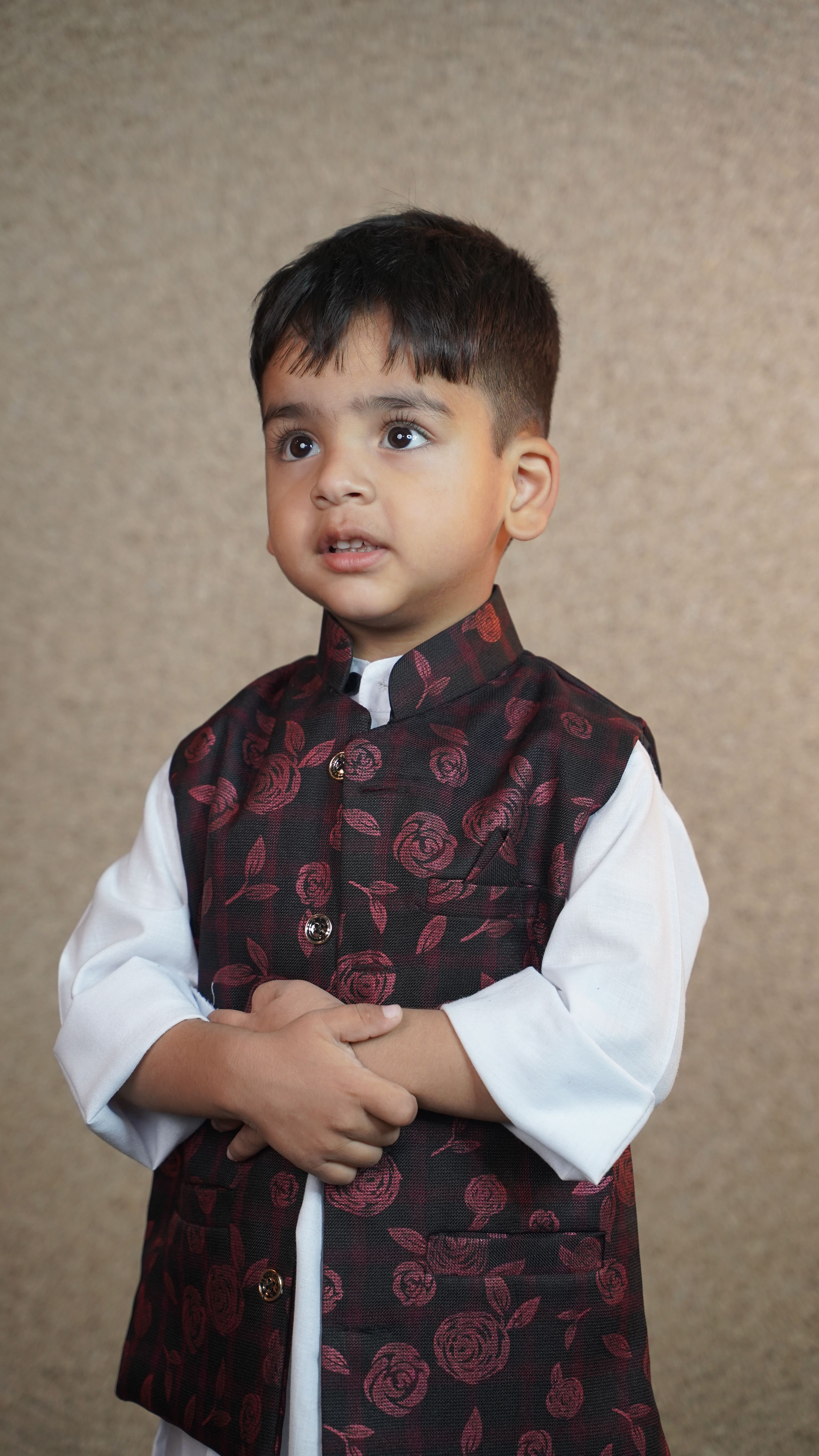 A young boy wearing traditional Kashmiri attire poses indoors with a thoughtful expression.