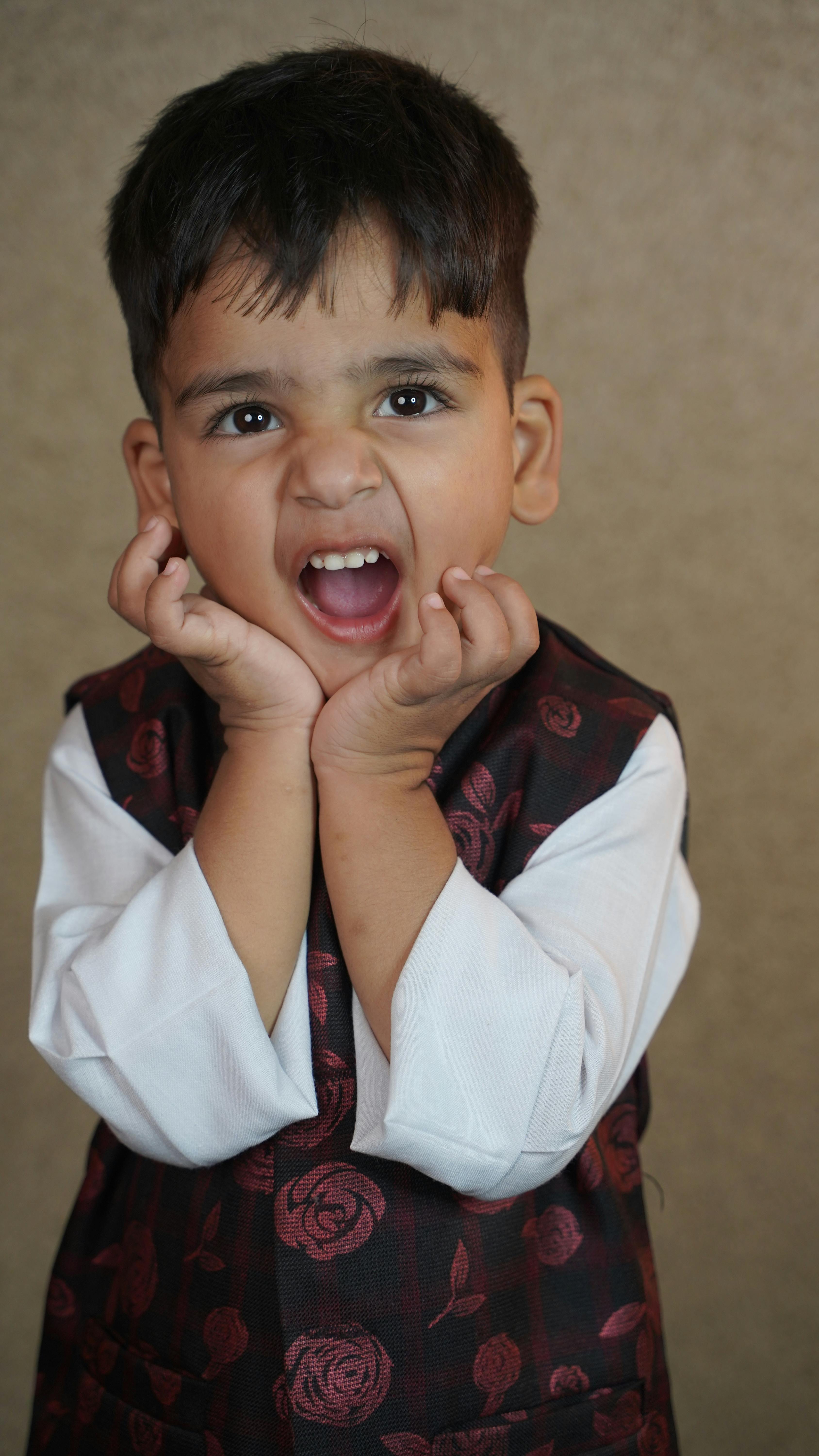 A cute young child in formal attire expressing a joyful and playful emotion indoors.