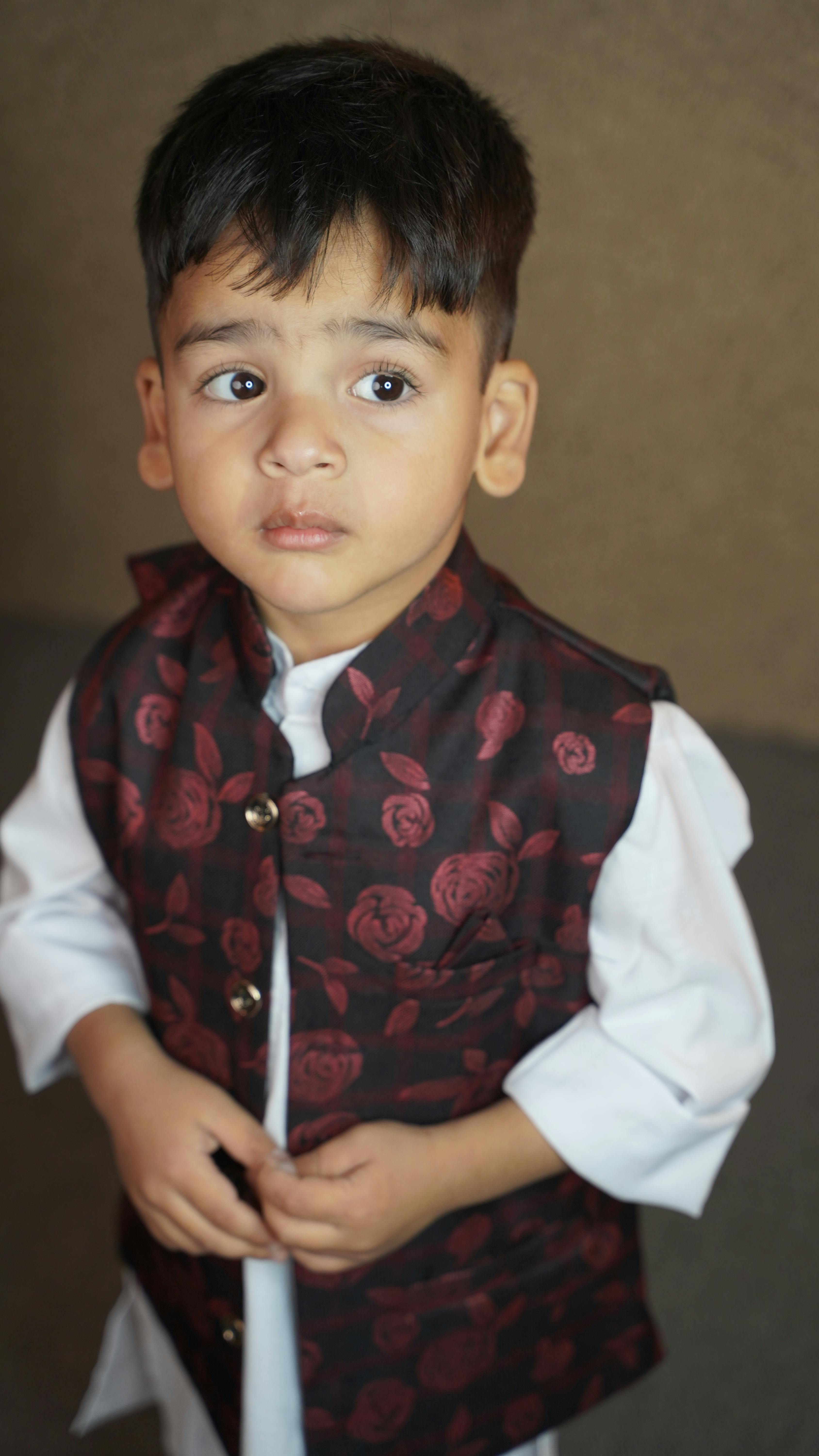 A cute young boy in traditional South Asian attire posing indoors.