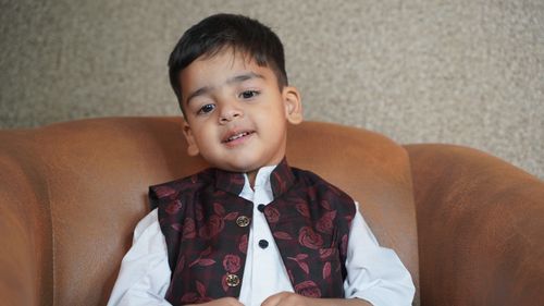Free Portrait of a smiling young child in traditional attire sitting on a sofa indoors. Stock Photo
