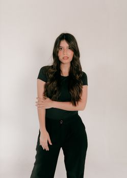 Elegant portrait of a young woman with long hair in a black outfit, posing against a minimalist white background.