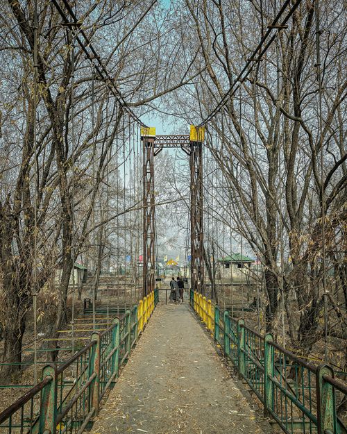 Free Two people cross a rustic bridge surrounded by bare trees, captured in a serene winter setting. Stock Photo