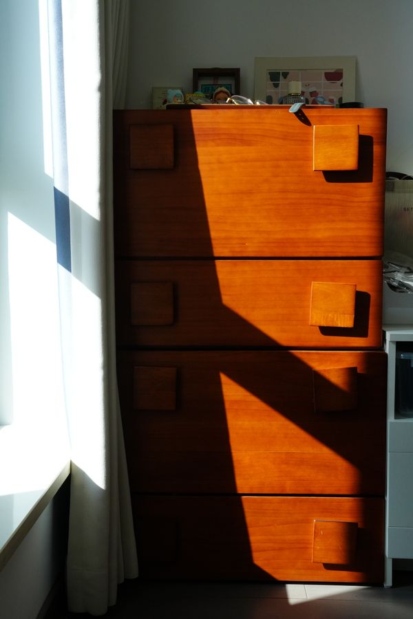 Slim wooden cabinet lit by raking sunlight — photo by Leila Chen on Pexels