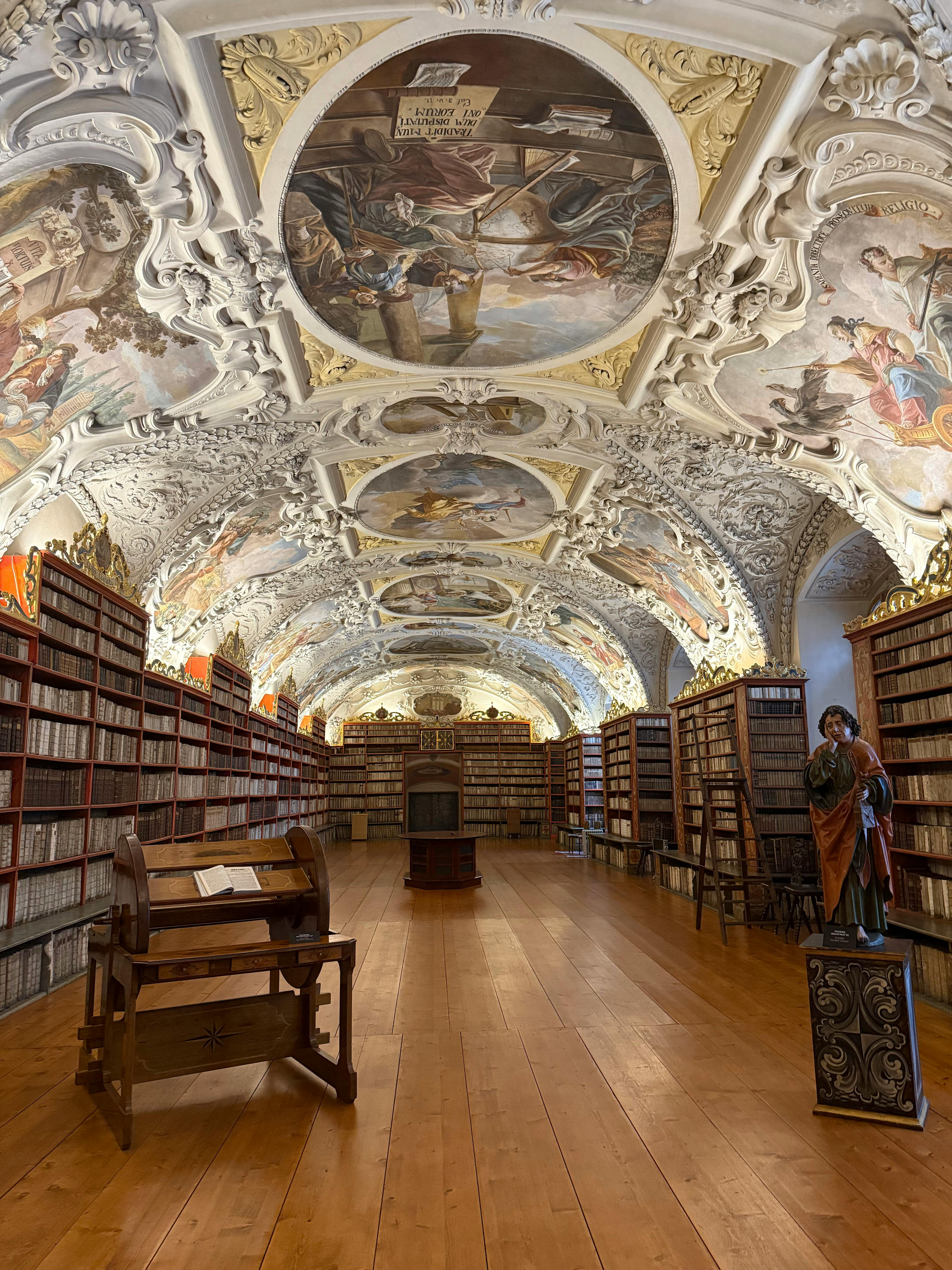 Stunning view of an ornate historical library with beautiful fresco ceilings and wooden bookshelves.