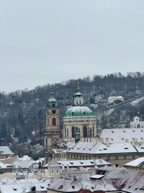 Free Winter scene of Prague's historic architecture covered in snow with a hill backdrop. Stock Photo