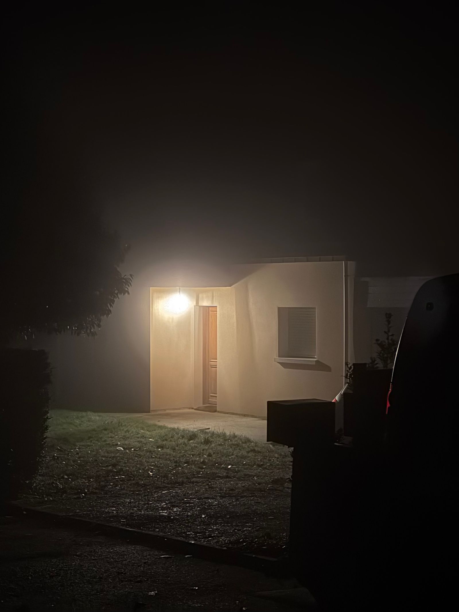 Entrée de maison éclairée par une seule lampe par une nuit de brouillard