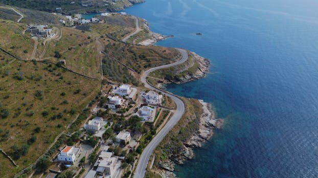 Scenic aerial view of winding coastal road and sea in Syros, Greece, showcasing natural beauty.