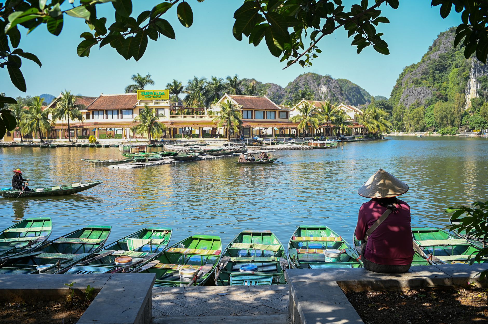 A tranquil riverside scene with traditional Asian boats and a person in a conical hat.