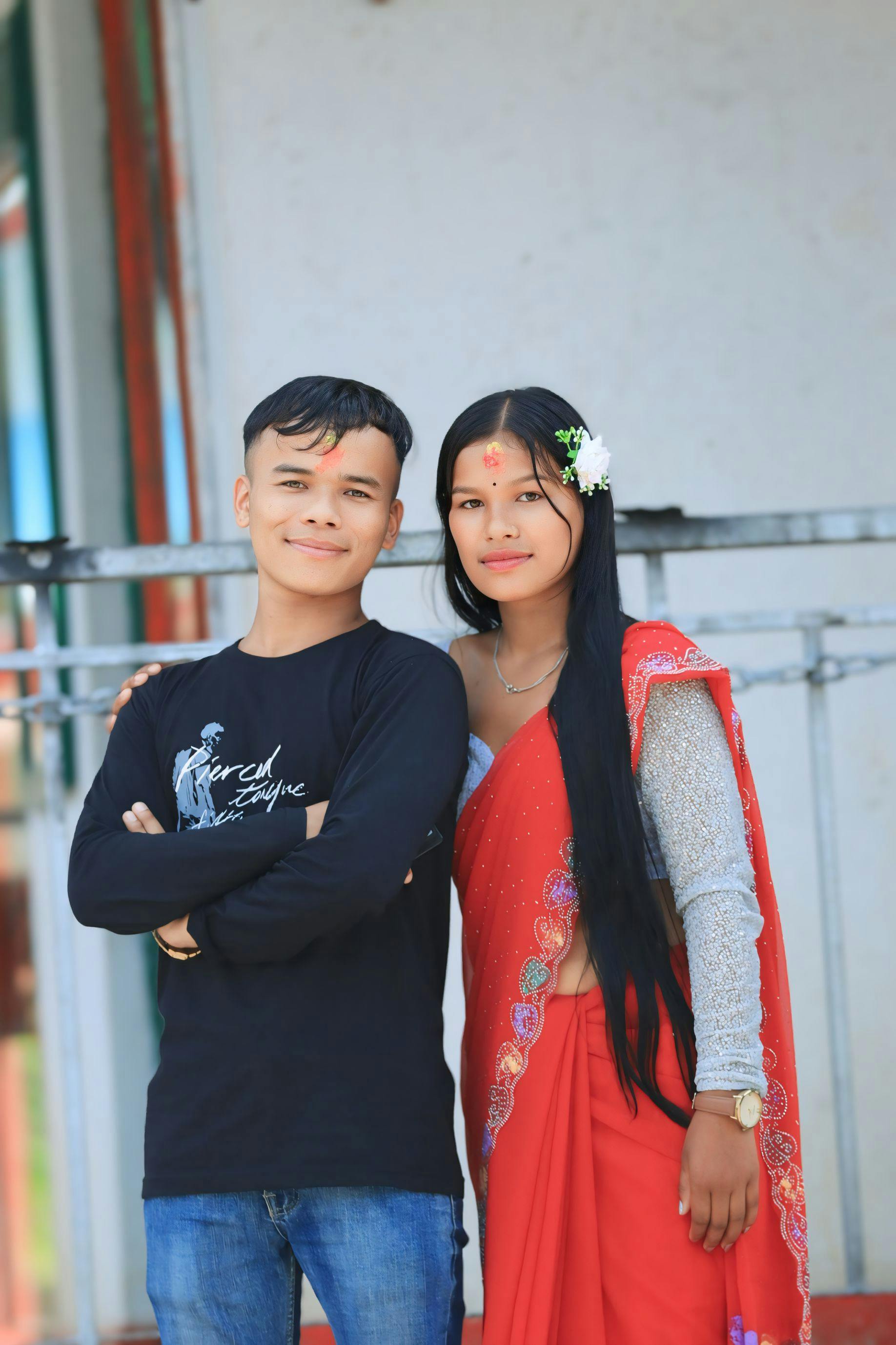 A smiling young couple in traditional and casual clothes posing outdoors.