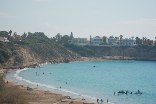 Beautiful beach scene with clear turquoise waters, sandy shore, and cliffside homes under a bright sky.