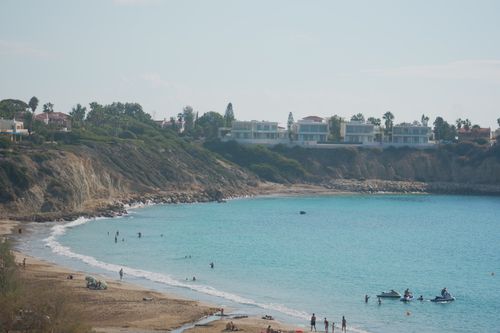 Free Beautiful beach scene with clear turquoise waters, sandy shore, and cliffside homes under a bright sky. Stock Photo