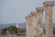 Ancient stone columns with a lighthouse in the background under a clear sky.