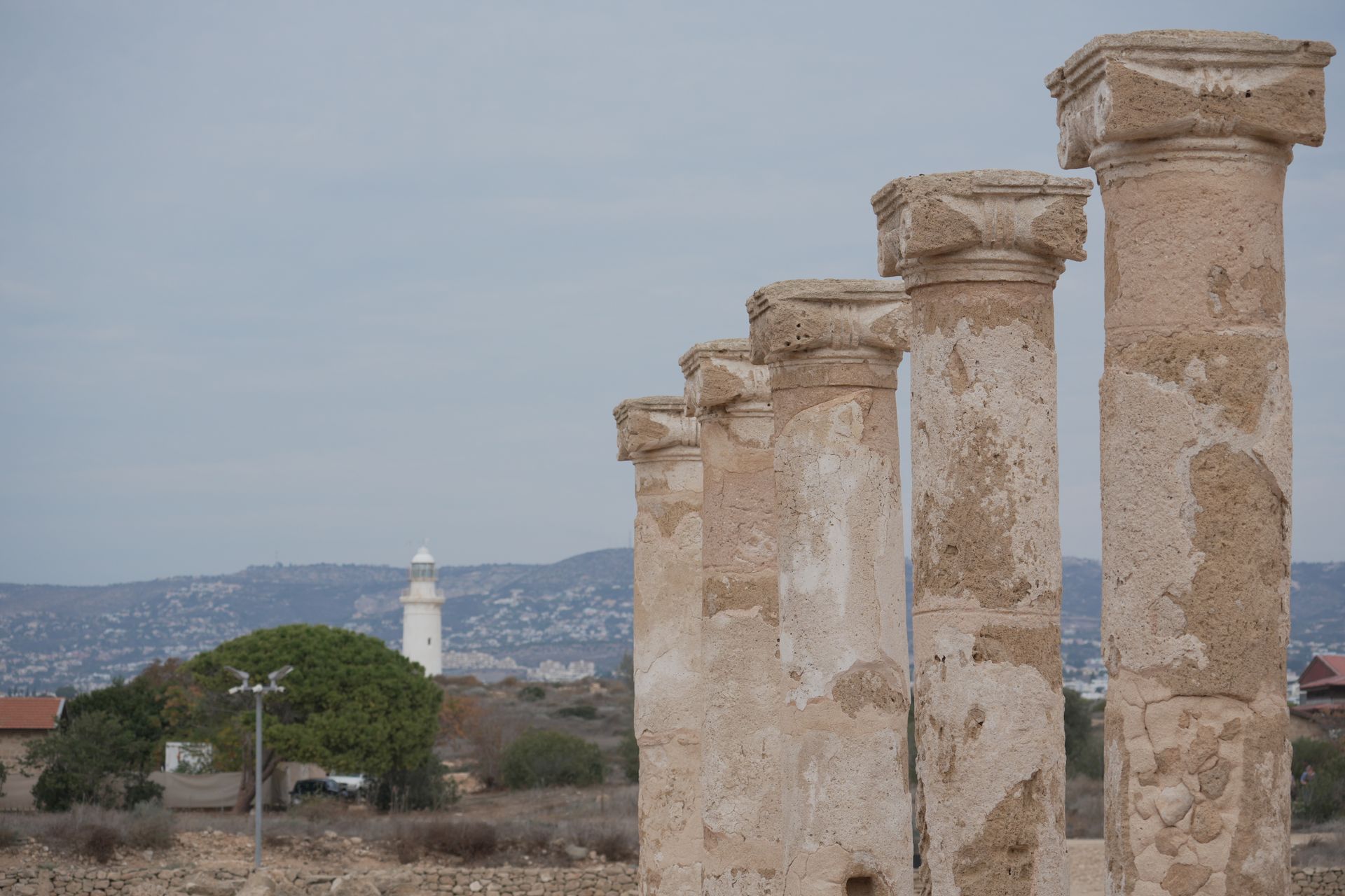 Ancient stone columns with a lighthouse in the background under a clear sky.
