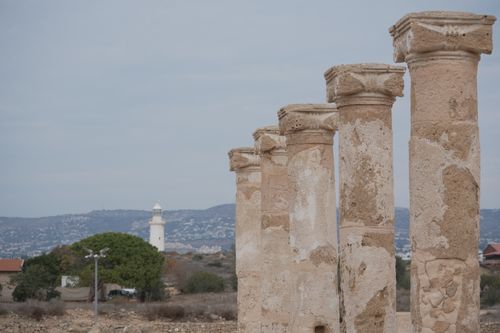 Free Ancient stone columns with a lighthouse in the background under a clear sky. Stock Photo