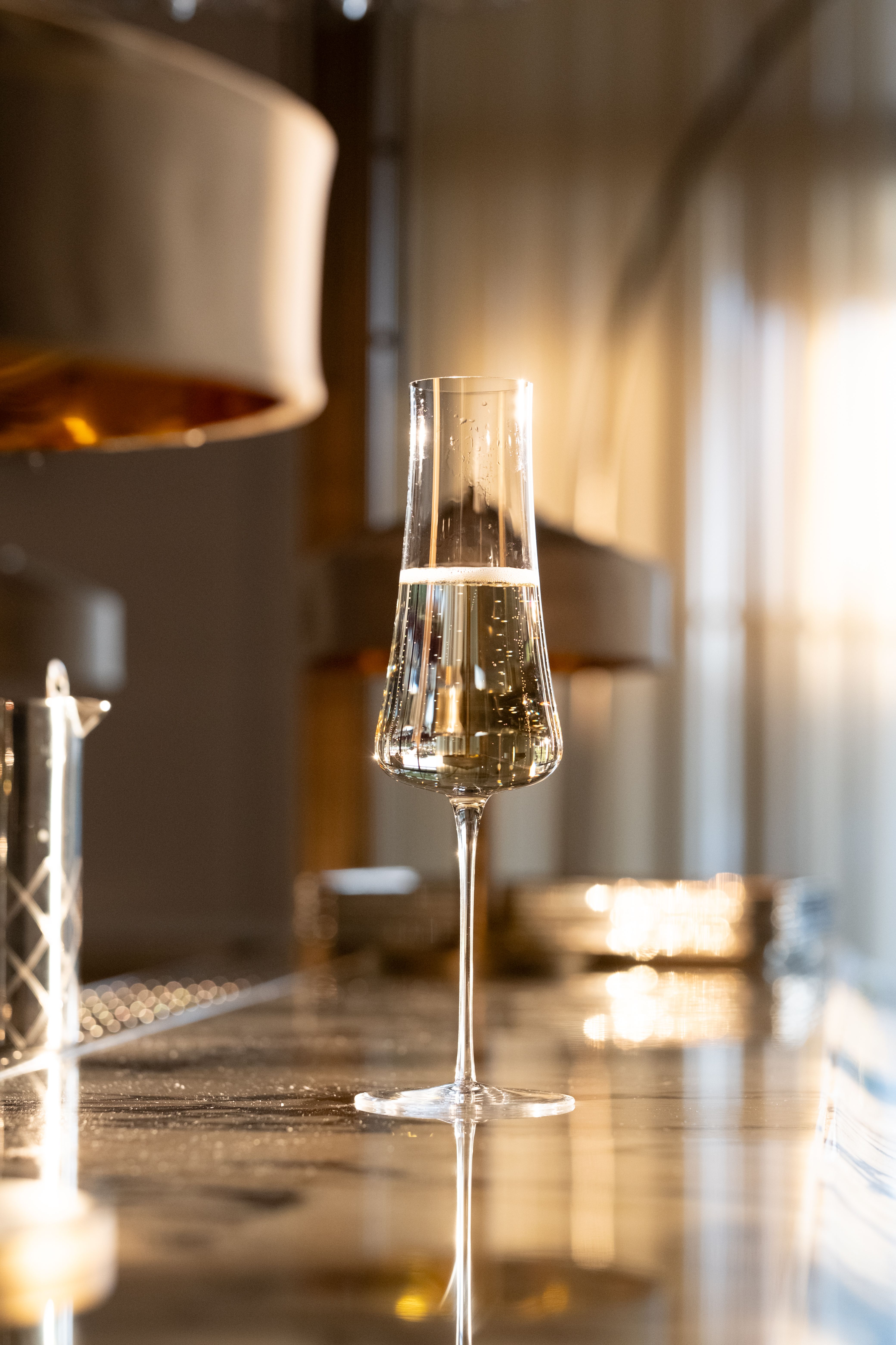 Chic champagne flute glistening on a marble bar top with gentle evening sunlight.