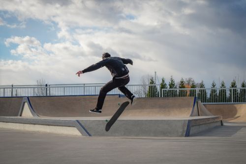 Free A skateboarder executes a mid-air trick at an outdoor skatepark under a cloudy sky. Stock Photo
