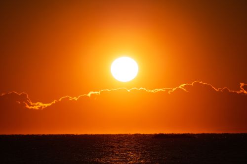 Free Stunning orange sunset over the ocean with light clouds on the horizon. Stock Photo