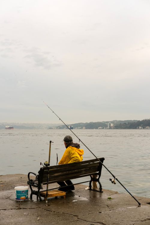 Free A solitary fisherman in a yellow raincoat sits by the Bosphorus on a rainy day in İstanbul. Stock Photo