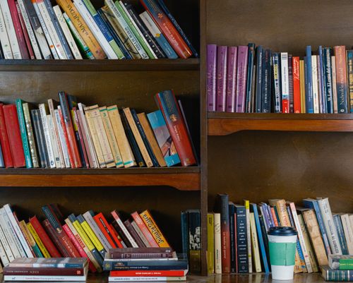 Free A warm library setting with filled bookshelves and a coffee cup on the table. Stock Photo