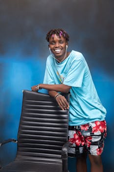 Cheerful young man leaning on chair with colorful fashion, exuding a joyful vibe.