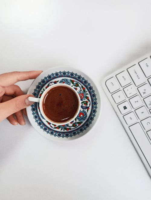 Free Hand holding Turkish coffee in an ornate cup on a white desk with keyboard. Stock Photo