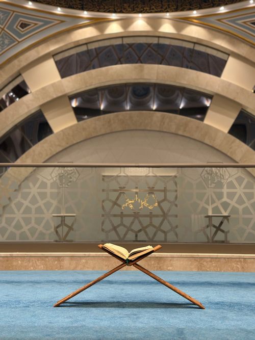 Free Spiritual view inside mosque, featuring Quran on stand against intricate architecture. Stock Photo